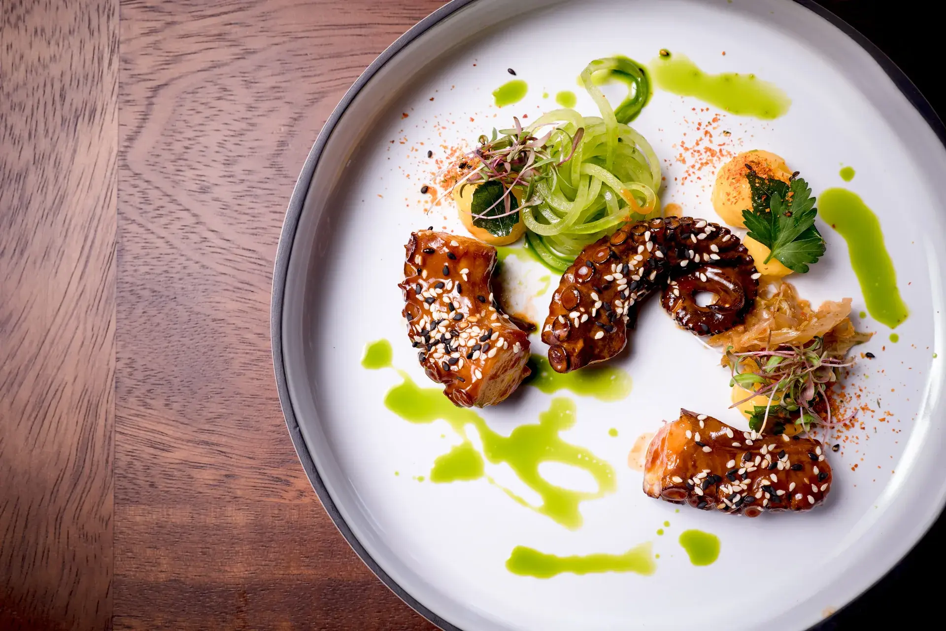 Sophisticated glazed octopus tentacles with spiraled cucumber and green puree on a minimalist plate