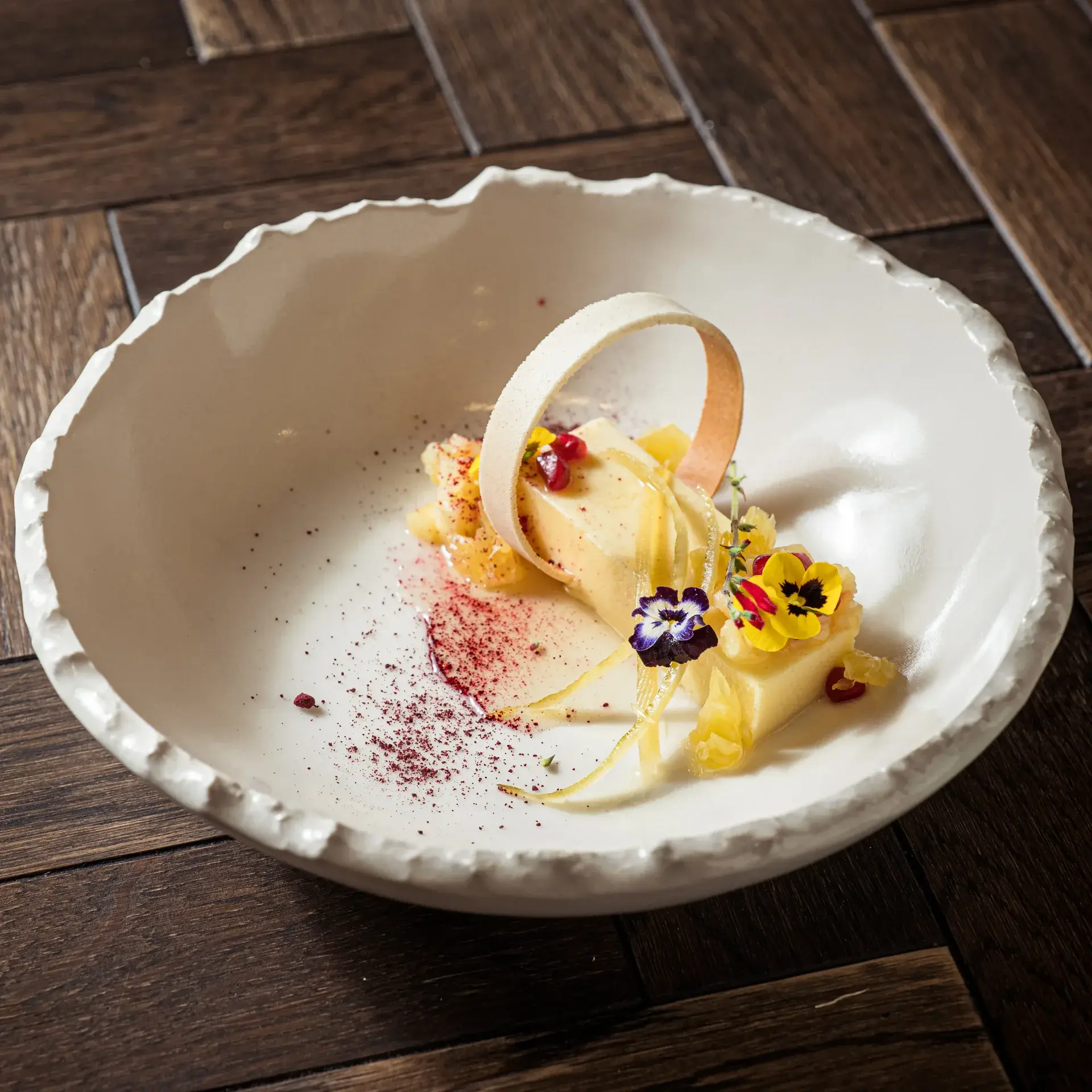 Elegant dessert plating featuring a white semifreddo, chocolate ring, edible flowers, and pomegranate seeds
