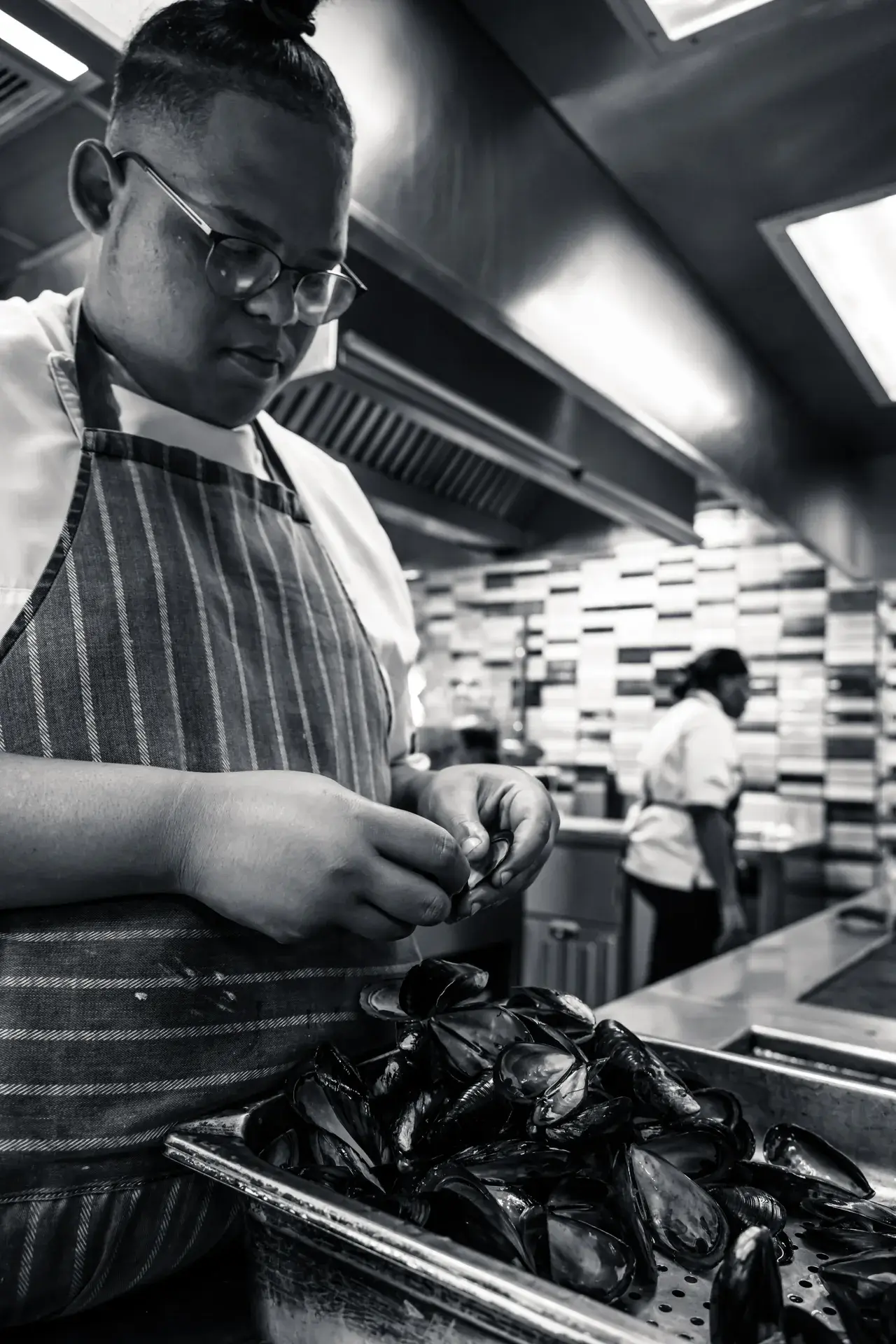 Black and white dramatic shot of a focused chef preparing fresh black mussels in a busy kitchen