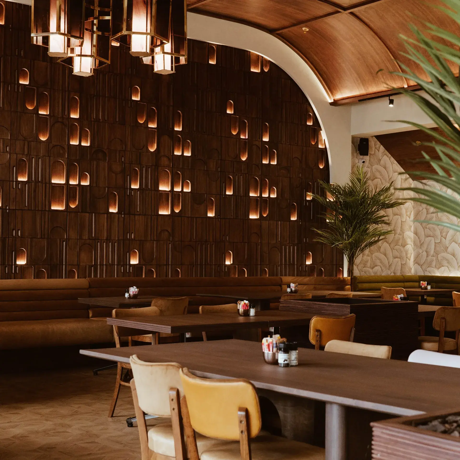 Luxurious restaurant interior featuring curved wooden wall cutouts, brown leather banquettes, and warm lighting