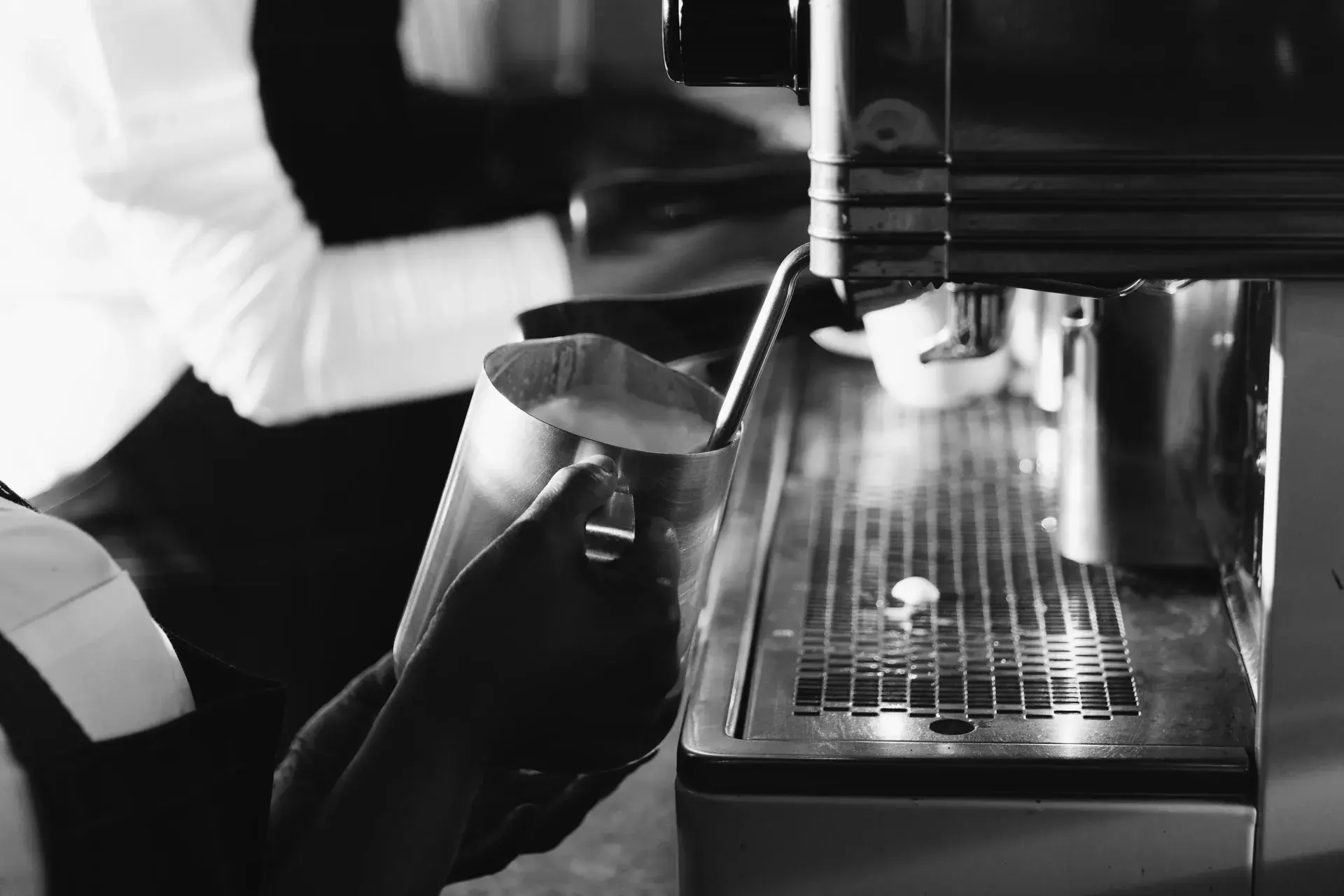 Black and white close-up of a barista expertly steaming milk at an espresso machine