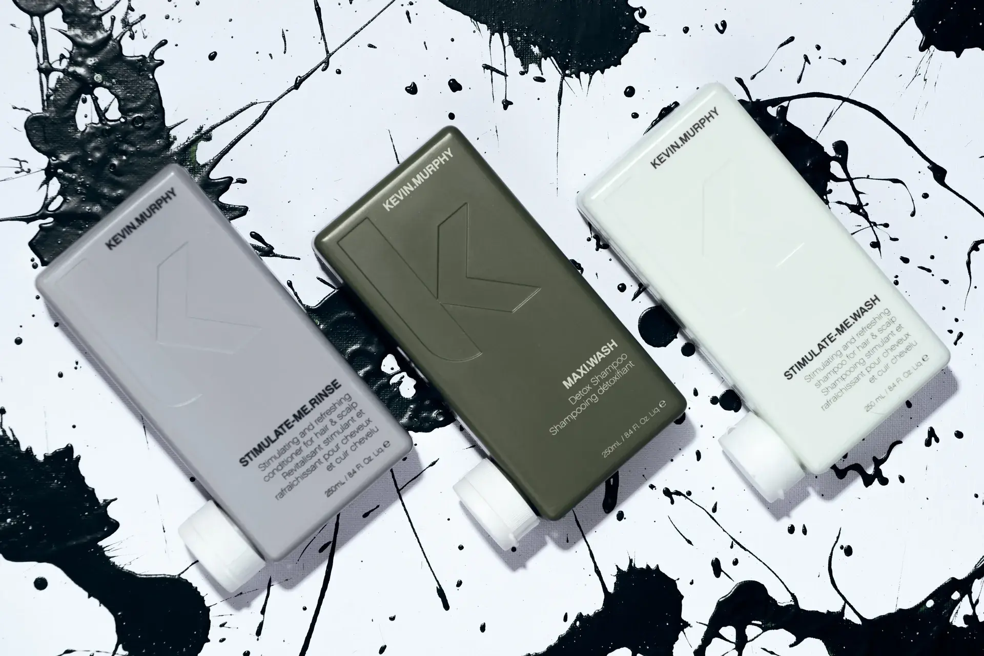 Three Kevin Murphy haircare bottles arranged dynamically on a white canvas with black paint splatters